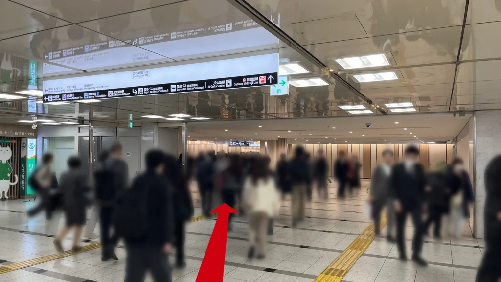 Alt:Signatureグラングリーンゲートタワーへのアクセス方法:多くの歩行者が行き交う地下通路で、左側の壁面に「りそな銀行」の緑色のサインとキャラクターイラストが表示されている様子。