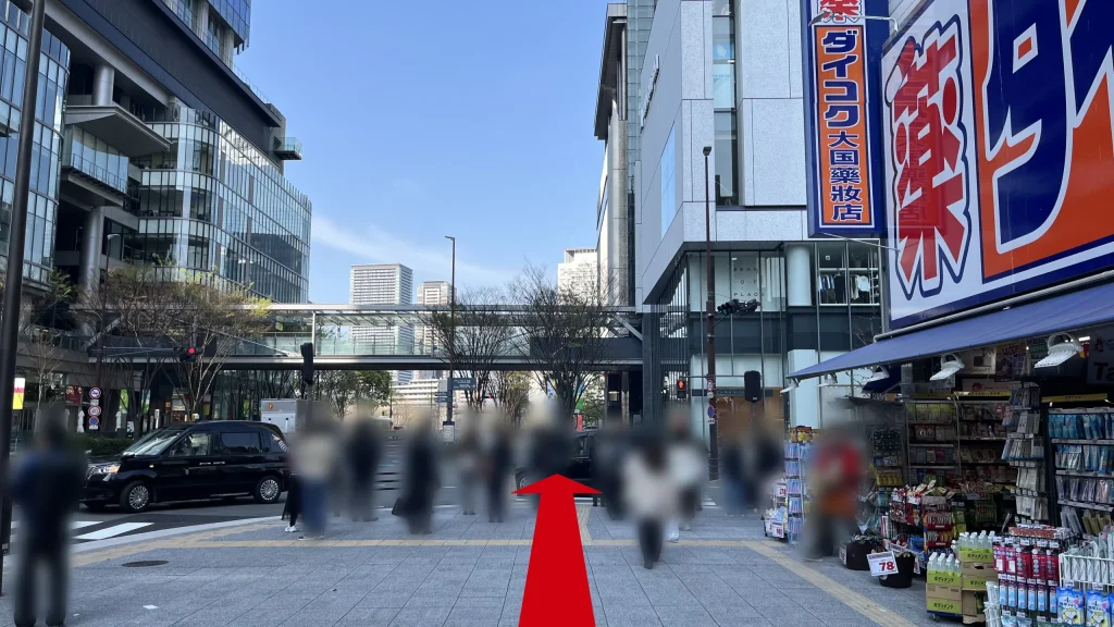 JAM BASEへのアクセス方法：右側に青とオレンジ色のダイコクドラッグの大きな看板があり、奥にビルを繋ぐ連絡通路が見える歩道の様子。