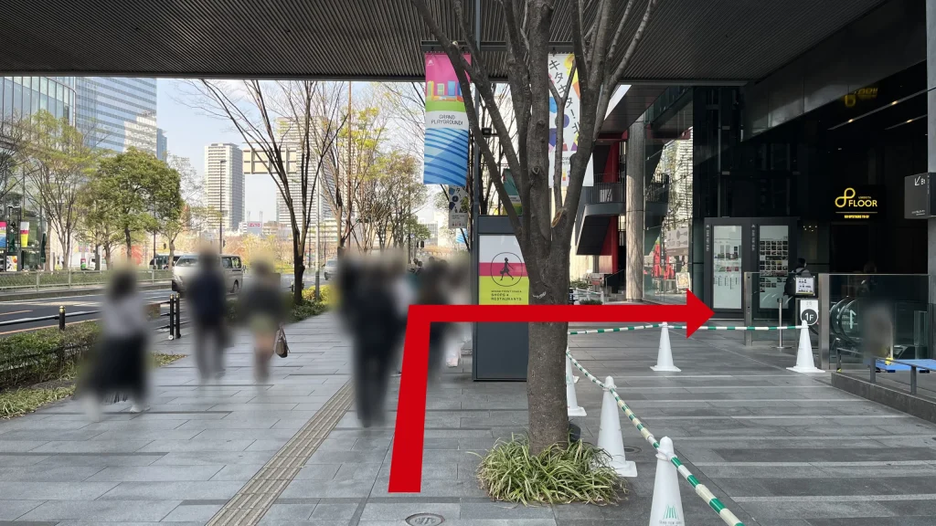 JAM BASEへのアクセス方法：右側にグランフロント大阪の案内看板と柱があり、頭上に大きな屋根が架かった通路を歩行者が進んでいる様子。