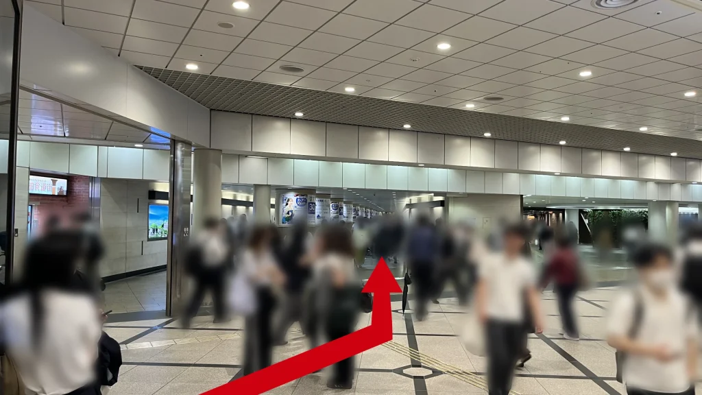 リージャス阪急ターミナルビルビジネスセンターへのアクセス方法:格子状の天井が続く地下風の通路を人々が歩いています。前方には丸い柱が並んでおり、その奥に動く歩道エリアが続いています。