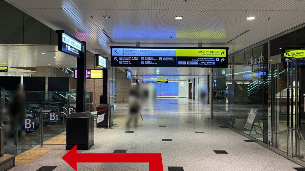 Compass Offices イノゲート大阪へのアクセス方法:上りエスカレーターの乗り口。右側には「ニューミュンヘン」の店舗、頭上には「うめきた公園方面」を示す黄色い案内板がありその手前で左に曲がる