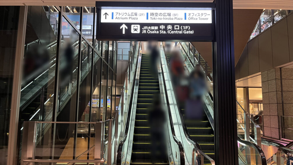 Compass Offices イノゲート大阪へのアクセス方法:上りエスカレーターの乗り口を正面から見た図 JR大阪駅中央口の矢印が書かれた看板が頭上に配置されている