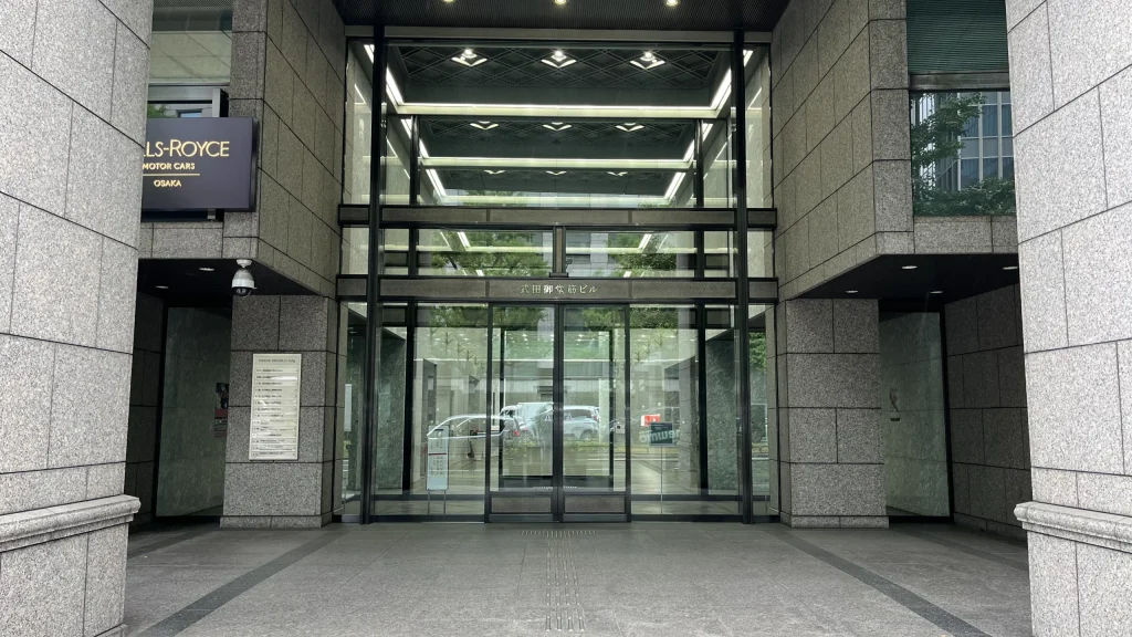 リージャス淀屋橋ビジネスセンターへのアクセス方法：ガラス張りのエントランスと、上部に武田御堂筋ビルと刻まれたビルの正面入り口。