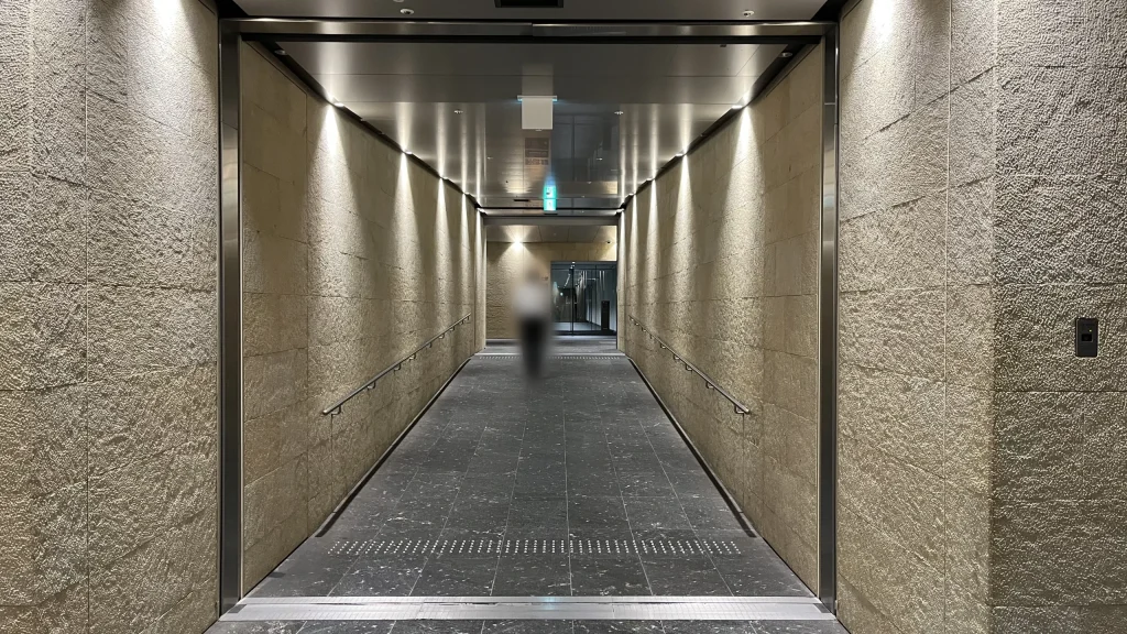 Signature大阪ダイビル本館へのアクセス方法：壁面から間接照明でライトアップされた、高級感のあるベージュの石造りの地下連絡通路がまっすぐ奥へと伸びています。