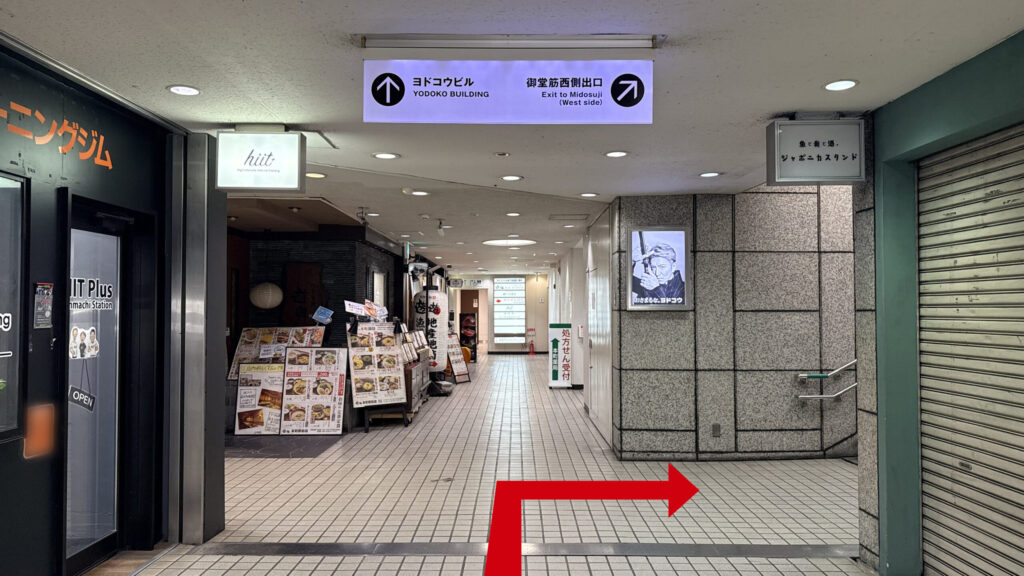 H¹O 本町Ⅱへの行き方：飲食店などが並ぶ地下通路の風景。頭上の看板に「ヨドコウビル 御堂筋西側出口」とあり、右奥に地上へ続く階段が見える。