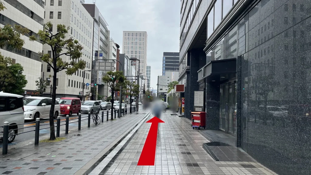 リージャス大阪国際ビルディングビジネスセンターへのアクセス方法：ビルが立ち並ぶ通り沿いの広い歩道。右側には黒い壁面のビルがある