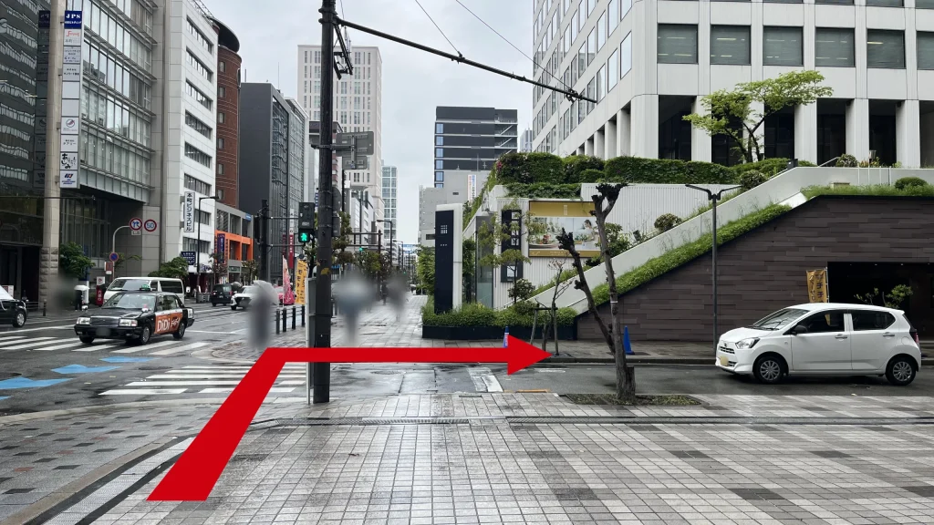 リージャス大阪国際ビルディングビジネスセンターへのアクセス方法：信号のある交差点の横断歩道。対向側には上部が緑化されたスロープ状の構造を持つ白いビルが見える。