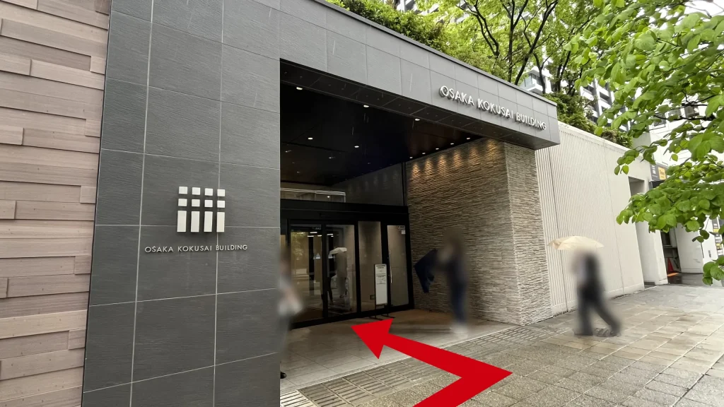 リージャス大阪国際ビルディングビジネスセンターへのアクセス方法：グレーの石壁に白いロゴマークと「OSAKA KOKUSAI BUILDING」の文字が刻まれたビルの広々としたガラス扉のエントランス。