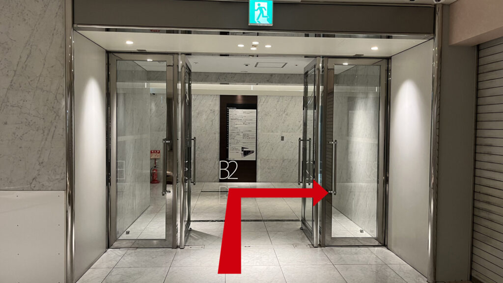 ZXY梅田への行き方：エレベーターホールへ向かう道　ガラス扉があり、奥にB2と書かれたビルの各階テナント一覧が掲示されている
