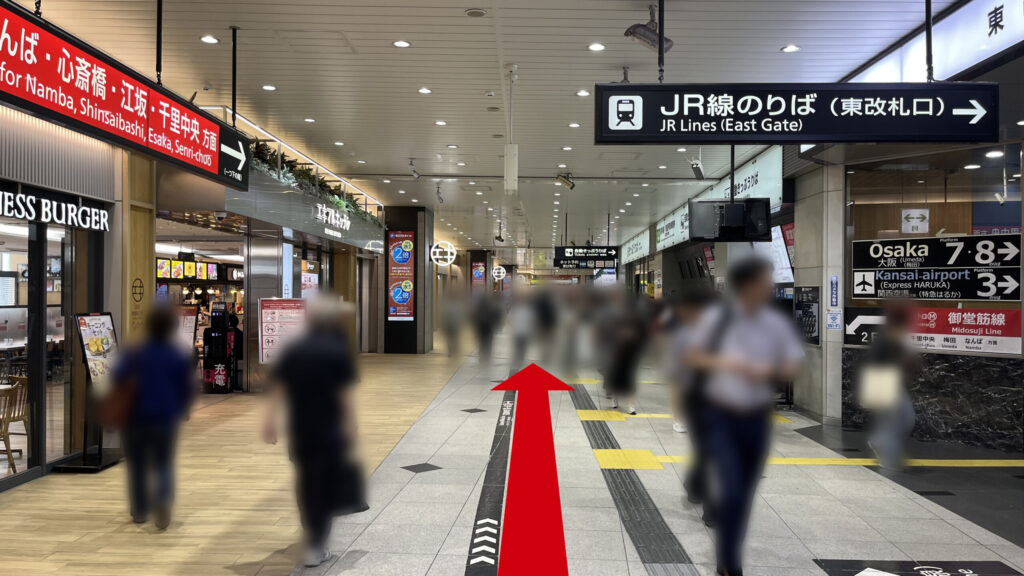 リージャス新大阪阪急ビルビジネスセンターへの行き方：JR線新大阪駅の東改札口を出た直後のコンコース。右方向へ誘導する頭上の案内看板があり、多数の歩行者が行き交っている。