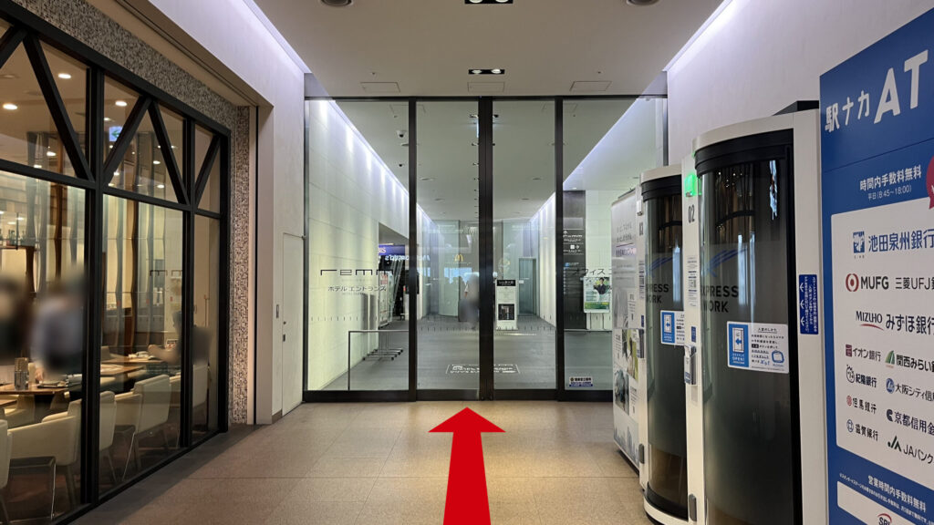 リージャス新大阪阪急ビルビジネスセンターへの行き方：通路の奥にあるガラス張りのホテルのエントランスドアと、手前右側に駅中リモートブースと駅ナカATMの端末が並んでいる