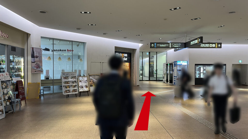 リージャス新大阪阪急ビルビジネスセンターへの行き方：エスカレーターを上りきった先にある広い屋内通路。左側には飲食店のガラス壁が見え、正面奥にはガラス扉のエントランスが視認できる。