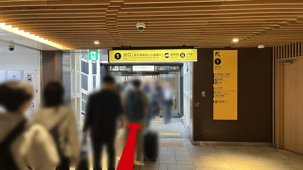 リージャス新大阪阪急ビルビジネスセンターへの行き方：地下通路の天井部分。「1番出口（新大阪阪急ビル連絡口）」と書かれた黄色い案内看板が大きく設置されており、直進方向を指し示している。