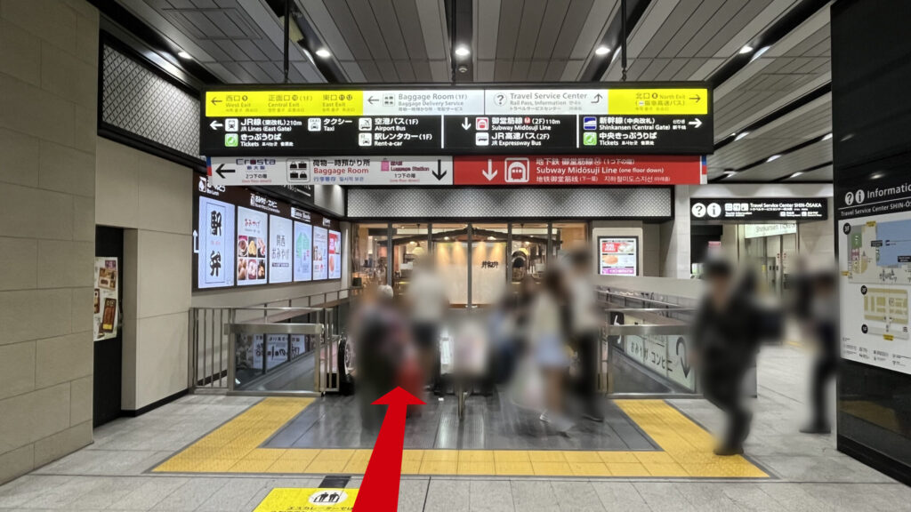 リージャス新大阪南ビジネスセンターへの行き方：御堂筋線への連絡通路のエスカレーター付近　向かいには飲食店、頭上には大きな案内板がぶら下がっている