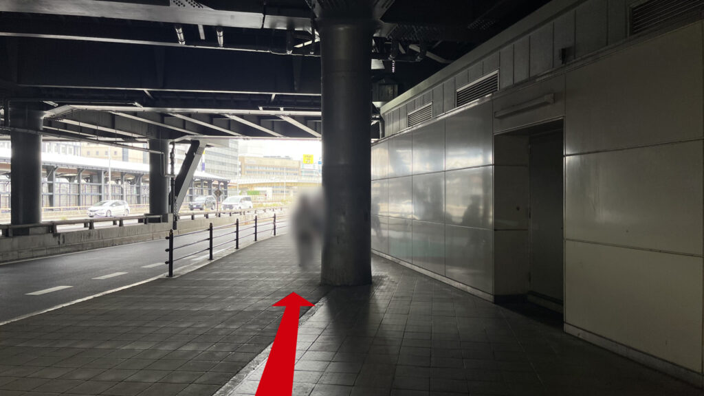 リージャス新大阪南ビジネスセンターへの行き方：6番出口を上に上がった時に見える景色　高架下の薄暗い通路が見える　左側に新御堂筋があり、車が走っている　右側には壁がある