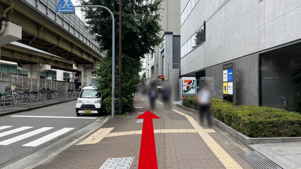 リージャス新大阪南ビジネスセンターへの行き方：歩道橋を下に降りた時に見える風景　茶色のタイルが敷かれた歩道の左に横断歩道、右にセブンイレブンが写っている　左に高架下の道路がある