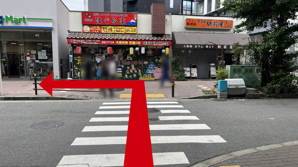 リージャス新大阪南ビジネスセンターへの行き方：横断歩道付近の写真　反対側の歩道沿いに「駅前屋」「はぐるま」と書かれた居酒屋、「ファミリーマート」が並んでいる