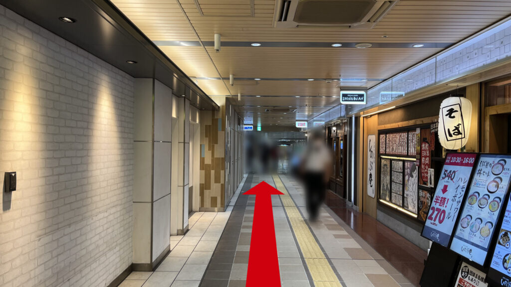 リージャス新大阪南ビジネスセンターへの行き方：飲食店の通路。左には壁、右には「そば」という提灯がぶら下がった飲食店が写っている